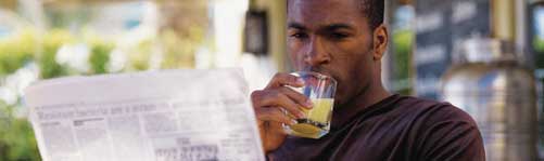 male drinking orange juice and reading paper